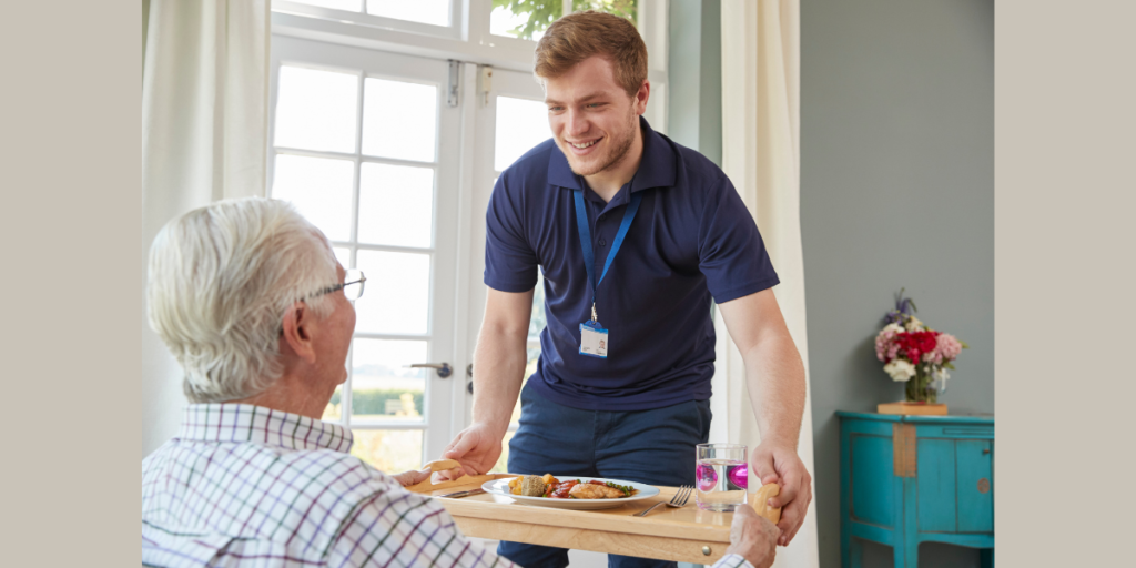 An image of an adult Care Worker serving an elderly gentleman dinner