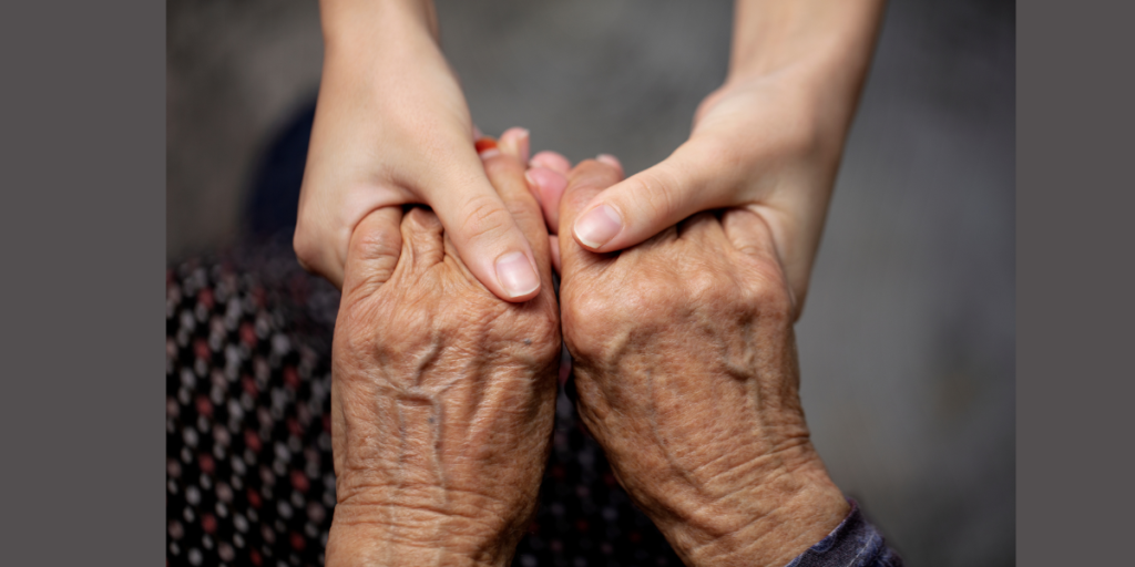 An image showing the hands of an adult care worker gripping the hands of an elderly lady