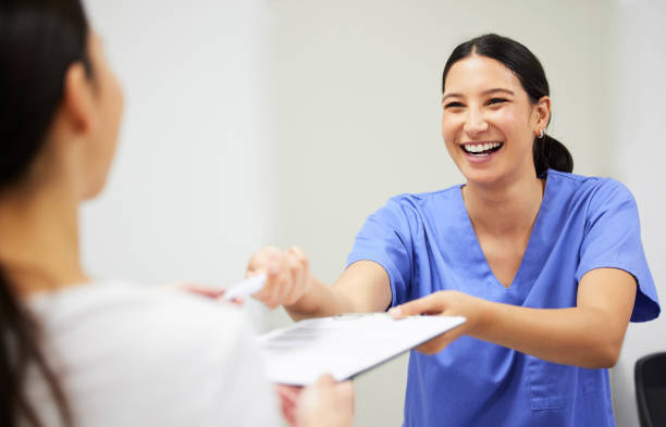 An assistant practitioner smiling and handing a clipboard to a patient